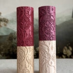Two Christmas ornament textured rolling pins in burgundy and ivory, featuring intricate baubles, bows, stars, and hanging beads.